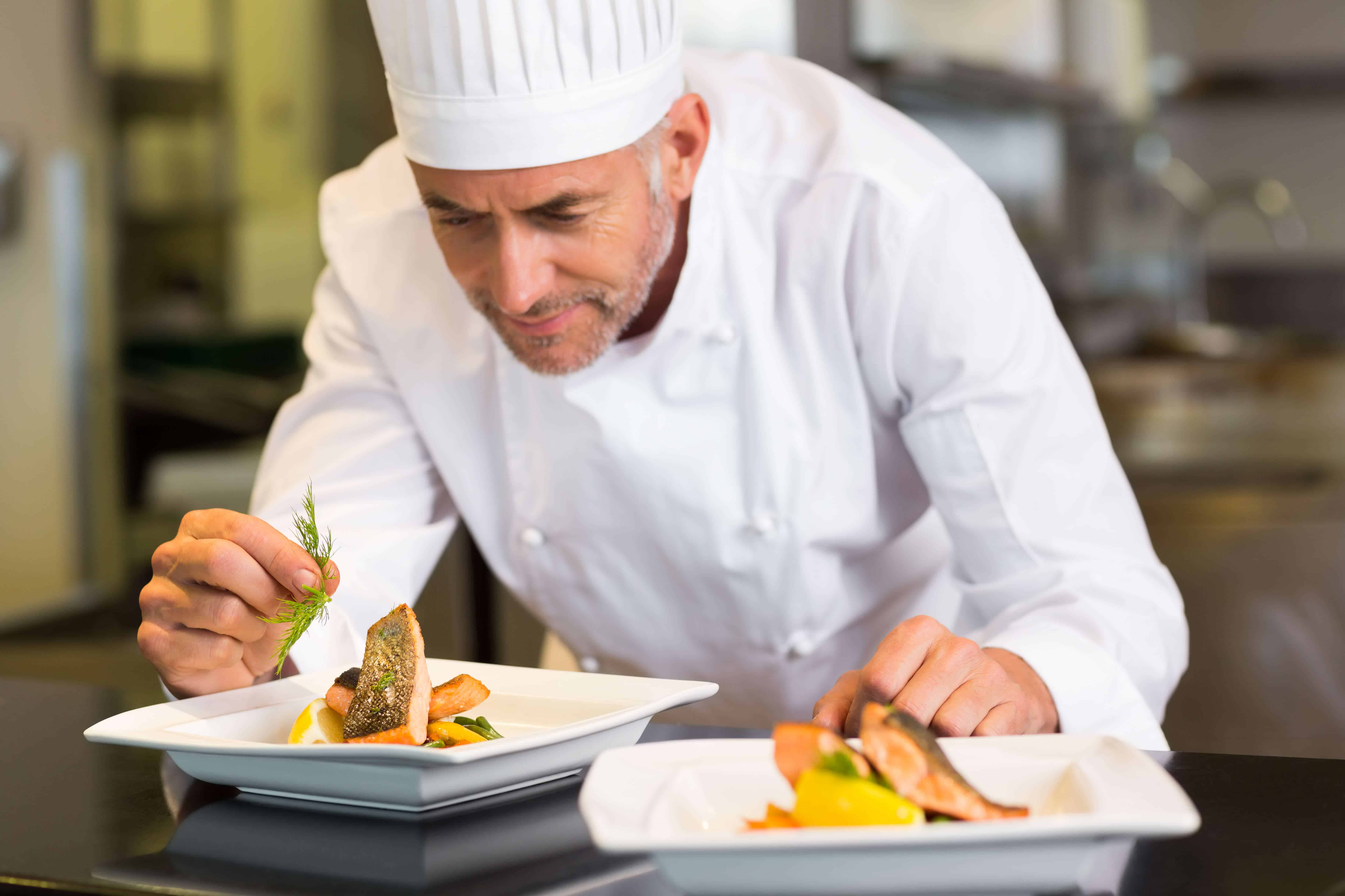 Closeup Of A Concentrated Male Chef Garnishing Food In The Kitchen closeup-of-a-concentrated-male-chef-garnishing-food-in-the-kitchen